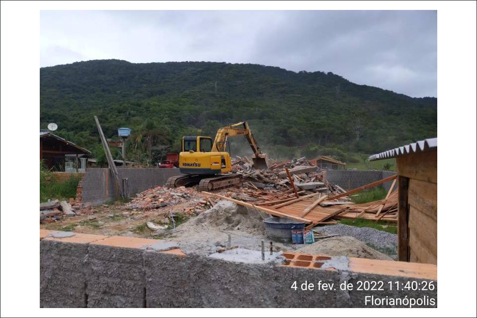 Na imagem uma máquina está demolindo casas dentro de um terreno