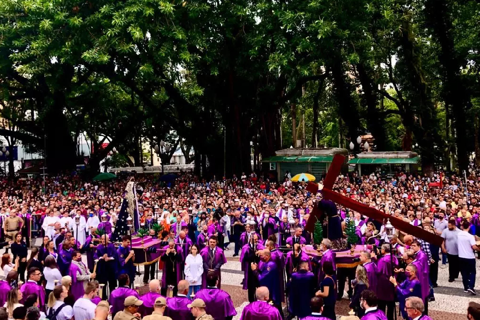 Foto colorida de uma multidão de pessoas carregando uma cruz