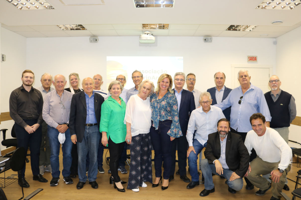 Foto colorida de uma grupo com dezenove pessoas homens e mulheres pousando para uma foto em um auditório com paredes brancas