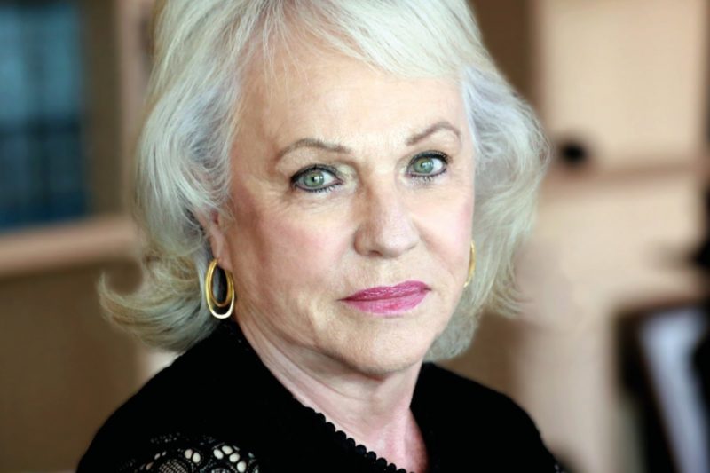Foto colorida de uma mulher com pele branca, cabelos grisalhos e vestido preto