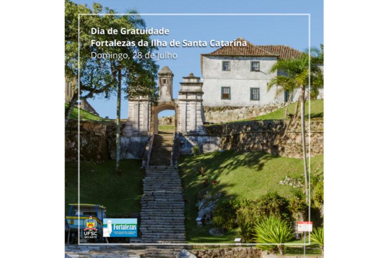 Uma escadaria de pedra leva a uma antiga fortaleza com paredes brancas e telhado de telhas, rodeada por um jardim gramado e árvores. No topo da escadaria, há um arco de entrada ornamentado com colunas e detalhes históricos. À esquerda, pode-se ver uma árvore grande e uma estrutura amarela menor. No canto inferior esquerdo da imagem, estão os logos da UFSC e do projeto Fortalezas de Santa Catarina. No topo, há um texto que diz: "Dia de Gratuidade Fortalezas da Ilha de Santa Catarina, Domingo, 28 de julho". A cena é iluminada por um céu azul claro e ensolarado.