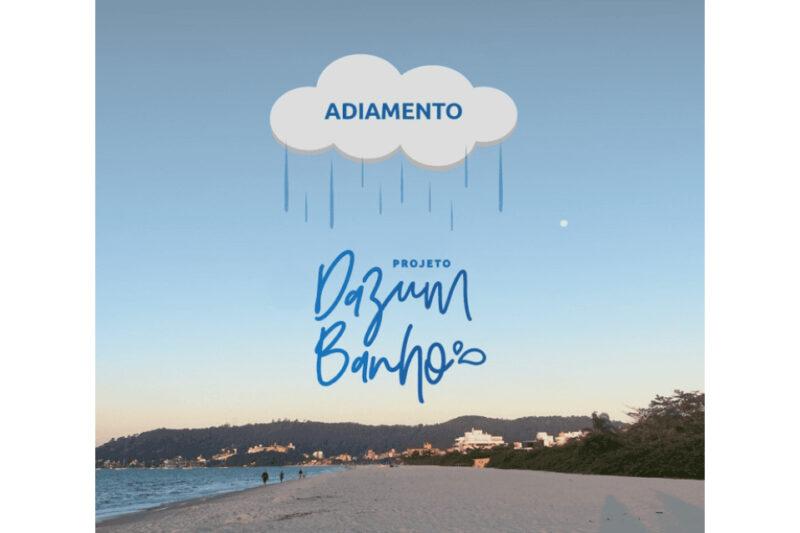 "Imagem com o fundo de uma praia ao entardecer, onde o céu está claro e sem nuvens. No horizonte, é possível ver a silhueta de montanhas e algumas construções ao longe. No topo da imagem, há uma ilustração de uma nuvem com gotas de chuva caindo, e a palavra 'ADIAMENTO' escrita dentro da nuvem. Abaixo da nuvem, o texto 'Projeto Dazumbanho' está em uma fonte cursiva azul, centralizado na imagem."