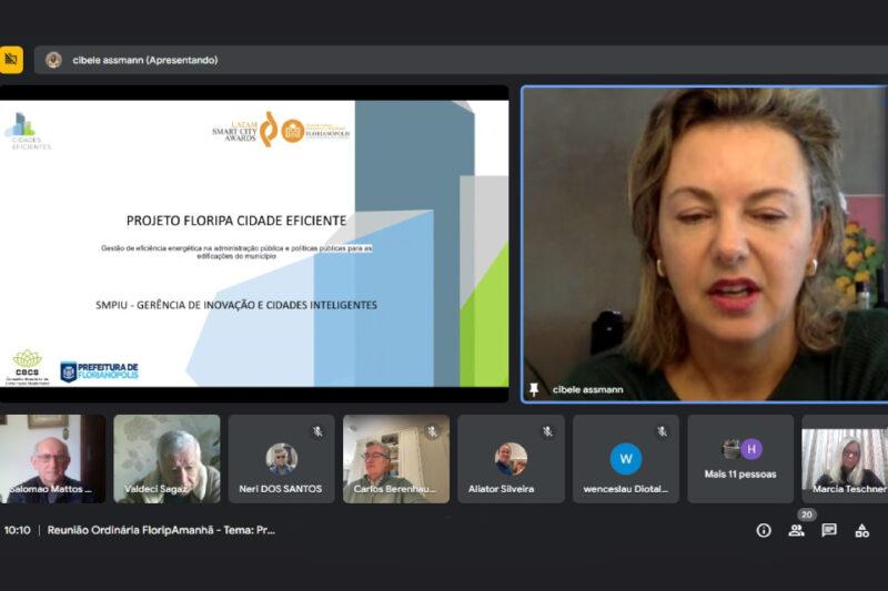 Captura de tela de uma reunião online da FloripAmanhã, mostrando a arquiteta Cibele Assmann à direita, falando sobre o 'Projeto Floripa Cidade Eficiente'. Na tela de apresentação à esquerda, há o título do projeto, com logos do 'Latam Smart City Awards', 'Florianópolis Cidade Criativa da Unesco', e da 'Prefeitura de Florianópolis'. Abaixo, na parte inferior da tela, há miniaturas de vídeo de outros participantes, incluindo Salomão Mattos Sobrinho, Valdeci Sagez, Neri dos Santos, entre outros, com o título da reunião visível: 'Reunião Ordinária FloripAmanhã.