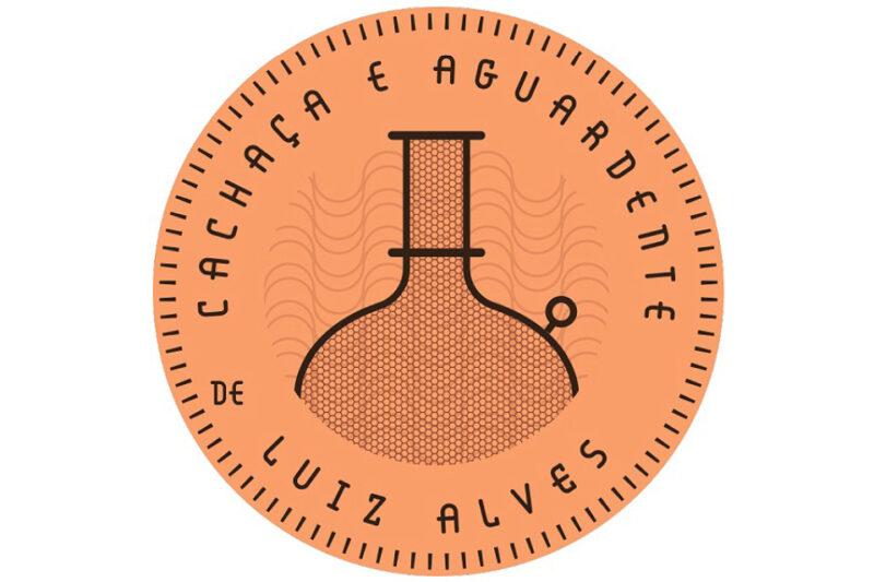 "Logotipo redondo em tons de laranja com borda pontilhada. No centro, há um desenho estilizado de um alambique, que é um equipamento tradicional para destilação de cachaça. Ao redor do desenho, está o texto 'Cachaça e Aguardente de Luiz Alves' em letras maiúsculas pretas, disposto em um formato circular seguindo a borda do logotipo."