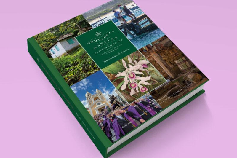 Livro de capa dura com fundo verde escuro e várias imagens ilustrativas relacionadas a Florianópolis, como uma orquídea, uma igreja, uma procissão religiosa, uma casa colonial e paisagens naturais. O título, em destaque no centro da capa, é “Orquídeas Nativas de Florianópolis: Contribuições ao Conhecimento das Orchidaceae Catarinenses”, de Marcelo Vieira Nascimento. A lombada e as bordas também são verdes. O livro está apoiado sobre uma superfície rosa.