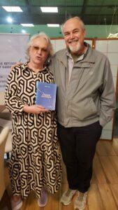 Fotografia de uma mulher segurando o livro “Cidade Dividida” ao lado de um homem sorridente.