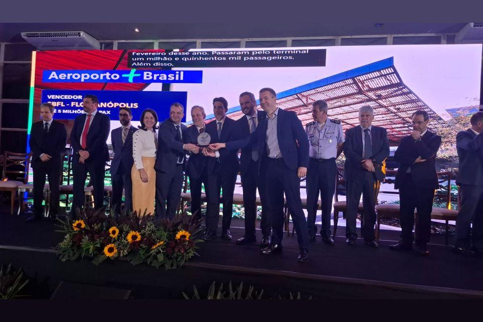 Cerimônia premia o Aeroporto de Florianópolis; grupo de treze pessoas posa sorrindo no palco.