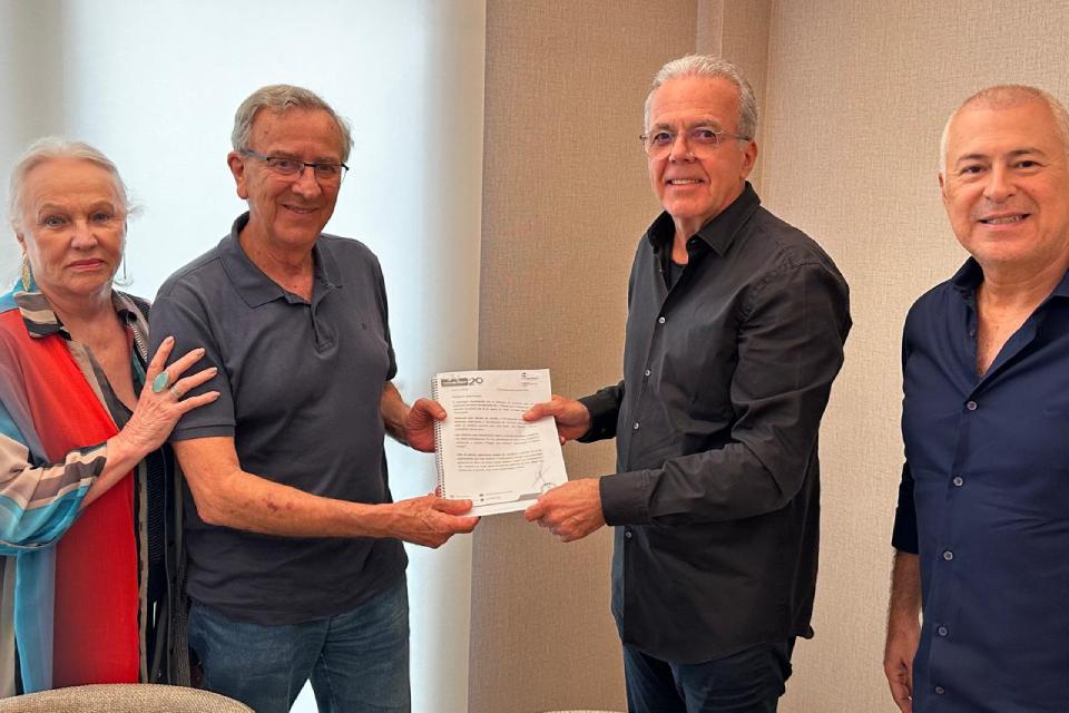 Quatro pessoas sorridentes posam em ambiente interno; duas delas seguram um documento impresso.