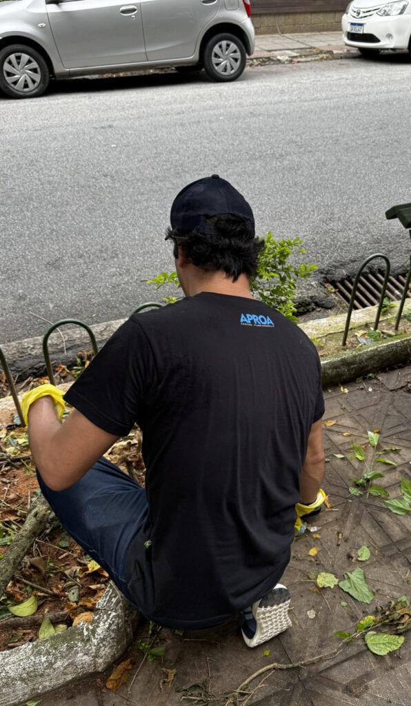 Voluntário com camisa da APROA cuida de plantas em canteiro na rua.