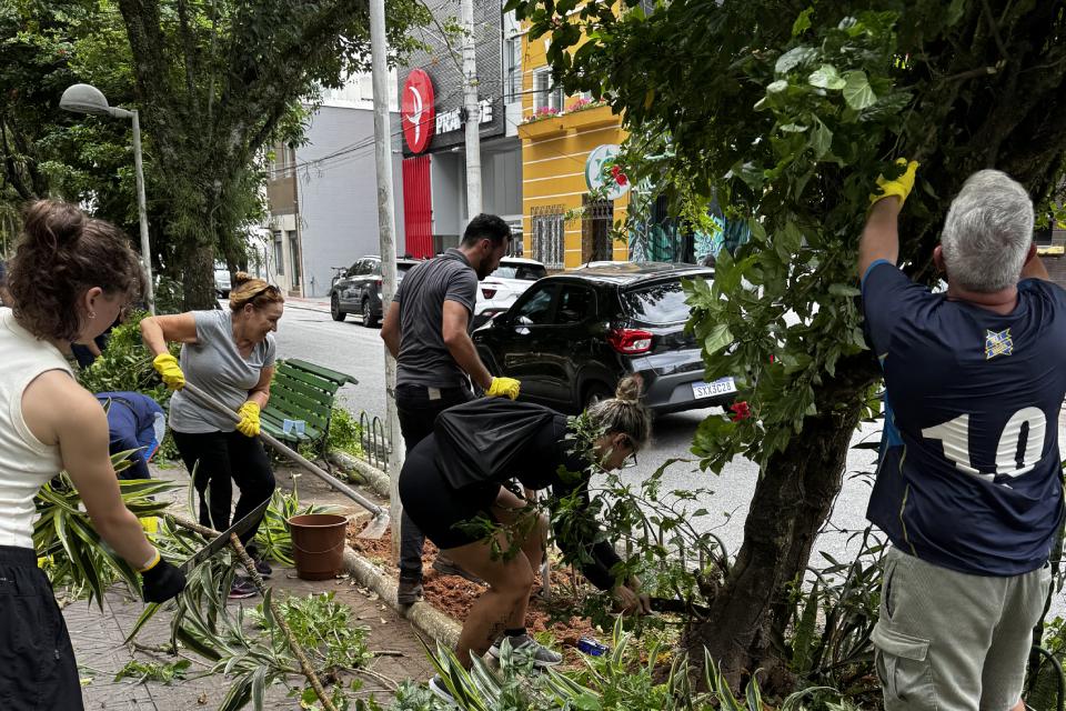 Grupo voluntário faz jardinagem em calçada urbana com ferramentas e luvas amarelas.