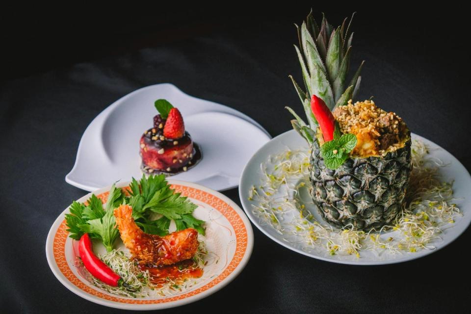 Prato artístico com camarão empanado sobre brotos e pimenta vermelha, arroz servido em abacaxi decorado com pimenta e hortelã, e sobremesa com frutas vermelhas sobre prato branco elegante.