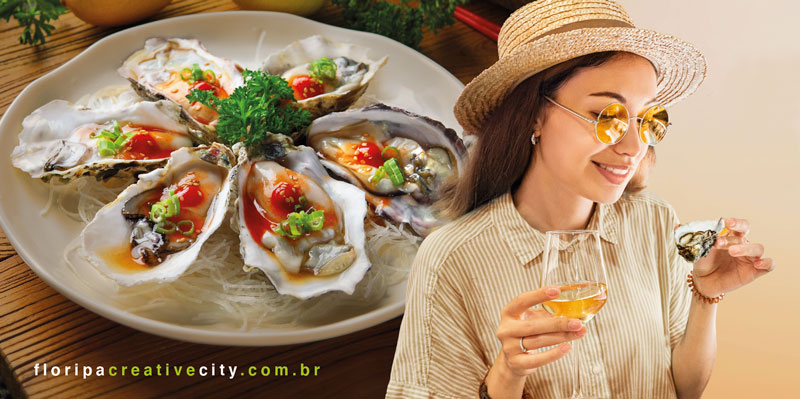 Prato com seis ostras decoradas com molho e cebolinha, ao lado de mulher sorridente segurando taça e ostra.