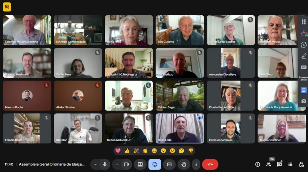 Tela de videoconferência com dezenas de pessoas distribuídas em mosaico, cada uma em seu ambiente, algumas com câmera ligada e outras com microfone desativado. Uma barra inferior exibe controles de chamada e emojis. 