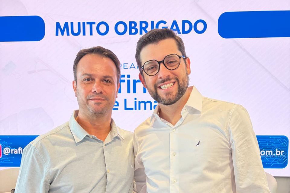 Fotografia de auditório com dezenas de pessoas sentadas em mesas redondas, voltadas para um palestrante diante de um telão. No fundo, lê-se: “Primeira reunião de dois mil e vinte e seis da Frente Parlamentar e sanção da lei do Reurb. Pauta: avaliação da agenda legislativa do último ano, dois mil e vinte e cinco, e plano de trabalho para dois mil e vinte e seis.”