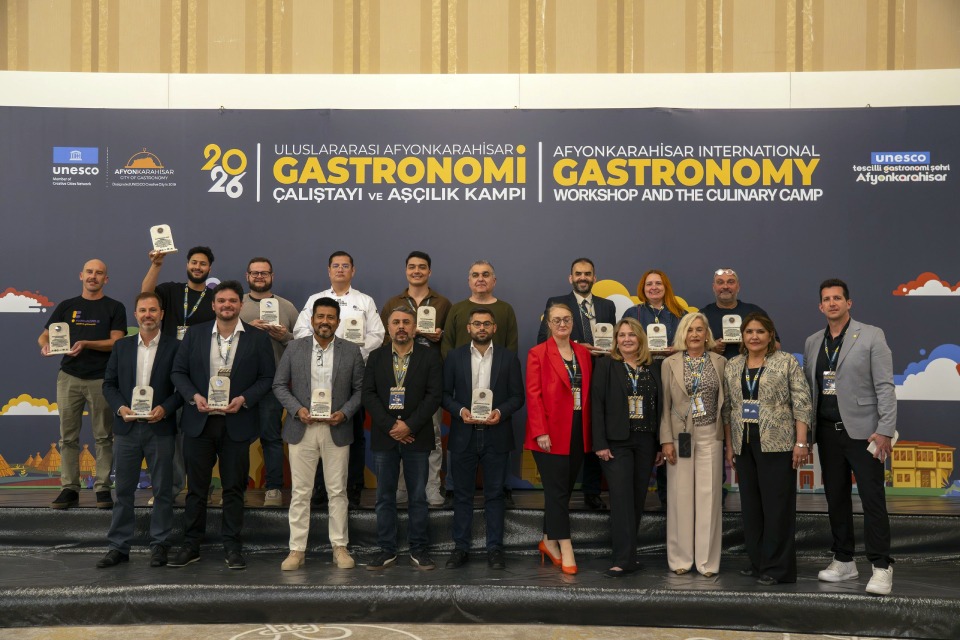 Fotografia de grupo em palco do Workshop Internacional de Gastronomia, com participantes segurando placas. 