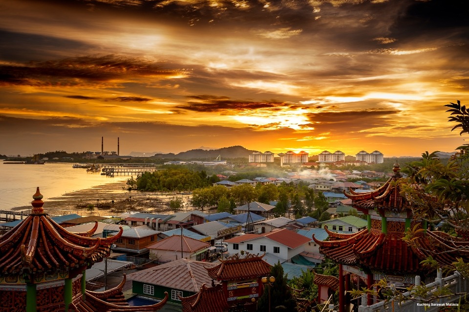 Fotografia de Kuching, na Malásia, ao pôr do sol, com telhados de templos chineses, rio e cidade ao fundo. Canva Pro/Getty Images