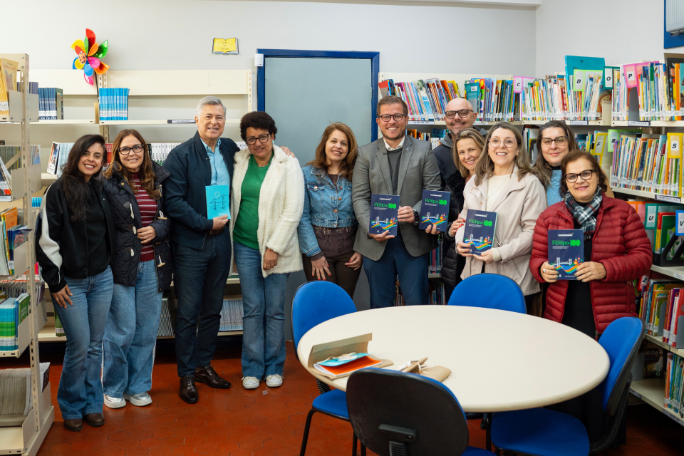 Fotografia mostra onze pessoas posando em uma biblioteca, diante de estantes de livros; cinco seguram exemplares de uma publicação sobre Florianópolis.