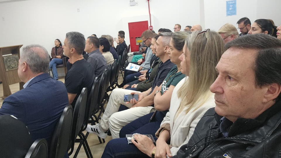 Fotografia de pessoas sentadas em fileiras durante uma apresentação, voltadas para a frente da sala.