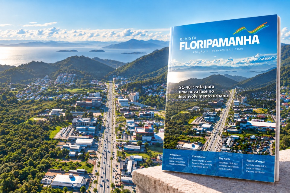 Montagem da revista FloripAmanhã sobre uma mureta, diante de paisagem com mar, montanhas e vegetação. Na capa: “Revista FloripAmanhã. Edição dois | Primavera | dois mil e vinte e seis. SC-quatrocentos e um: rota para uma nova fase no desenvolvimento urbano”. Abaixo: “Indicadores — Monitoramento expõe conquistas e desafios ambientais”; “Plano Diretor — Investimento privado financia infraestrutura e habitação social”; “Eixo Norte — Hospitais, clínicas e inovação fortalecem polo de saúde”; “Sapiens Parque — Ciência e negócios compartilham o mesmo território”.